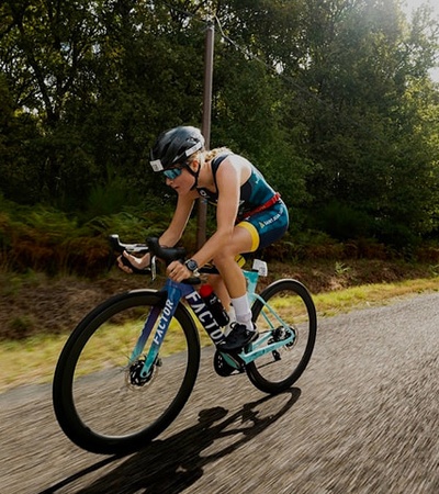A cyclist racing down a country road surrounded by trees.