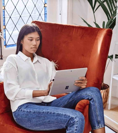 A woman sits on a red chair using a tablet in a stylishly decorated room.