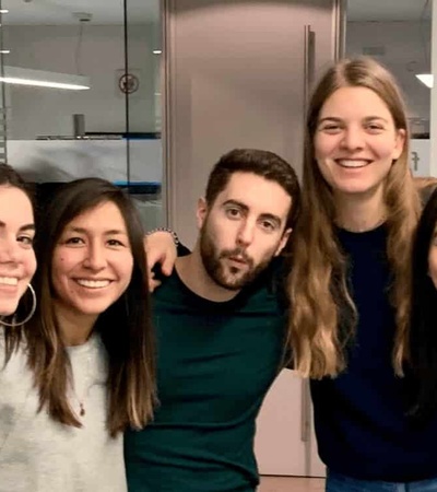 A group of six young adults smiling and posing together in an office environment.