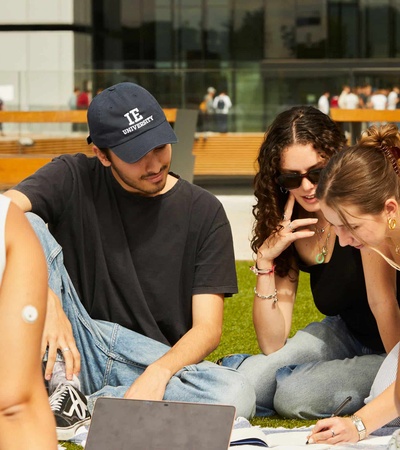 A group of young adults studying and discussing together outdoors on a grassy area.