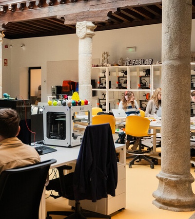 A modern workspace with people collaborating and using various technology in a bright, open environment.