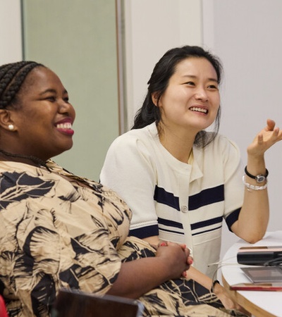 Two women are smiling and engaged in conversation at a workplace setting.