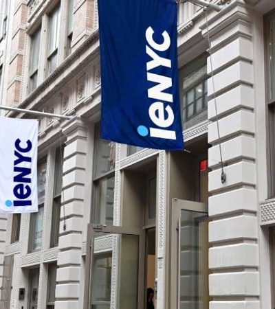 A view of a city street with large blue flags displaying 'ieNYC' hanging from a modern building facade.