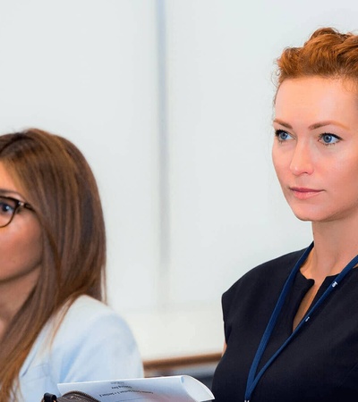 Two women attentively participating in a seminar, one with auburn hair and the other wearing glasses.