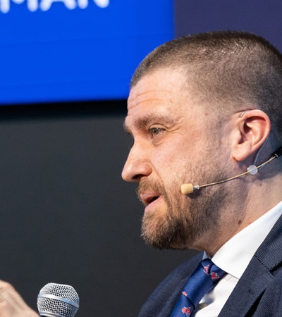 A man in a suit is speaking into a microphone at a conference.