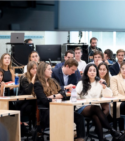 A diverse group of attentive students listening to a lecturer in a university classroom setting.