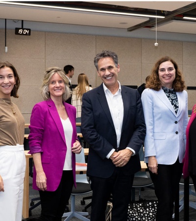 Five professionals, three women and two men, smiling in a conference room with chairs and tables in the background.