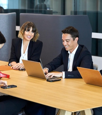 Four business professionals working and discussing around a table in a modern office setting.