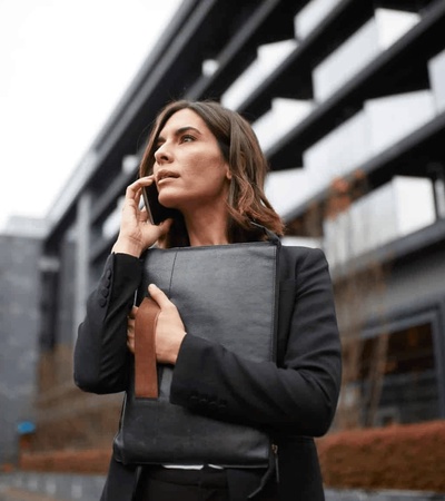 A professional woman holding a briefcase speaks on her phone outside a modern building.