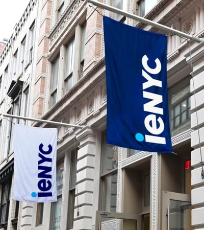 Blue and white flags with the text 'ieNYC' hang outside a building on an urban street.