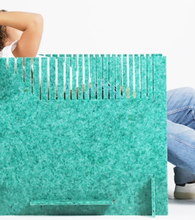 A woman sits behind a large turquoise shopping bag, her face obscured and only her arms and legs visible.