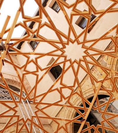 A complex geometric ceiling structure made of interlocking wooden beams.