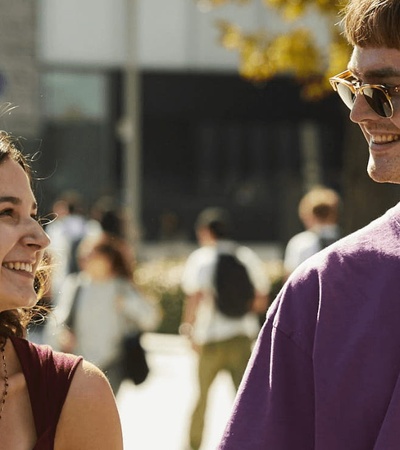 A young couple smiles and walks together in a lively outdoor setting.