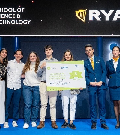 A group of young people proudly holding a large check on stage, flanked by flight attendants, at a Ryanair event.