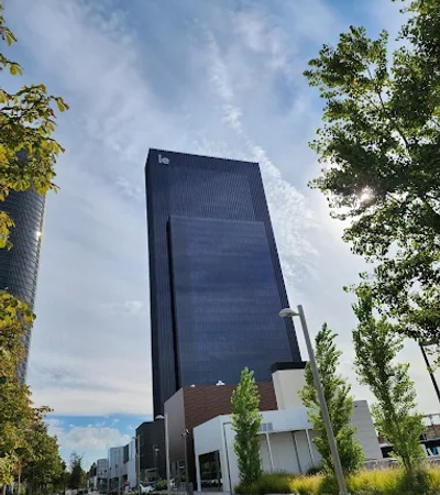 A towering modern building with a reflective facade and greenery surrounding it.