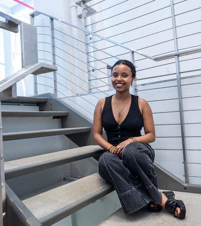 A young woman is sitting on the stairs in a modern indoor space.