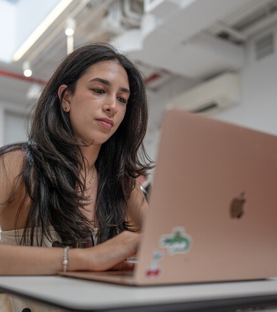 A young woman is working on a laptop in a modern classroom setting.