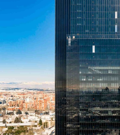 A modern glass building with a view of a snowy cityscape and distant mountains.