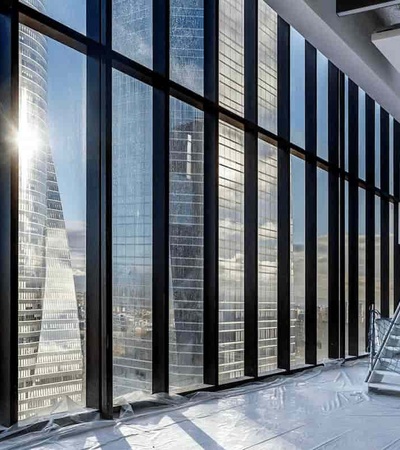 Modern interior space with large windows offering a city view, under construction with visible protective materials on the floor.