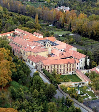 Aerial view of a large historical building surrounded by autumn-colored trees.