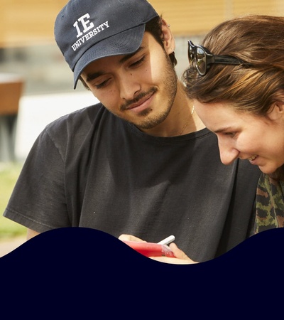 Two young people, a man and a woman, are smiling and looking at a smartphone together.