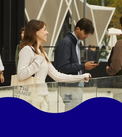 Young adults interact in a lively urban plaza, with some walking and others engaged in conversation.