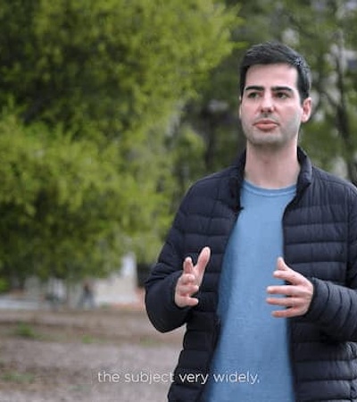 A man in a park is speaking, possibly captured during an interview or presentation.