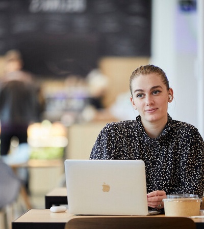 A woman sitting at a table in a café, focused on her laptop.