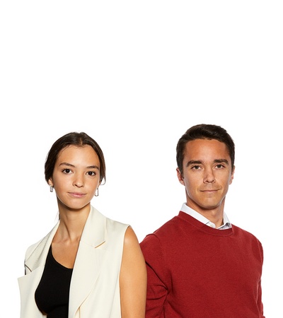 A man and a woman standing side by side in fashionable attire.