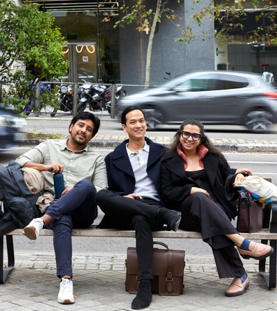 Three friends sitting on a bench by the street.