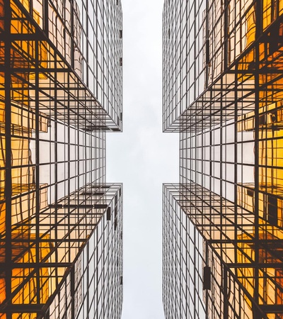 Looking upward between two symmetrical skyscrapers with a clear sky above and reflections on the glass facade.