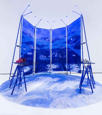A modern art installation featuring a blue backdrop with mountain imagery and two distinct tables.