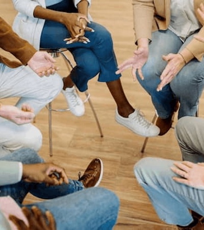 A group of people sitting in a circle, gesturing with their hands during a discussion or activity.