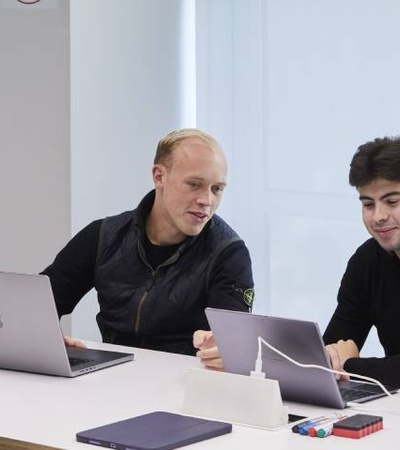 Two men working together on laptops in an office setting.