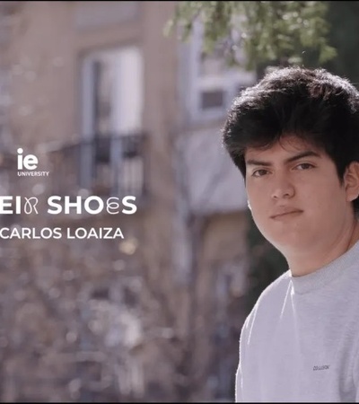 A young male stands outdoors with a thoughtful expression, promotional text for 'In Their Shoes with Carlos Loaiza' overlays the image.