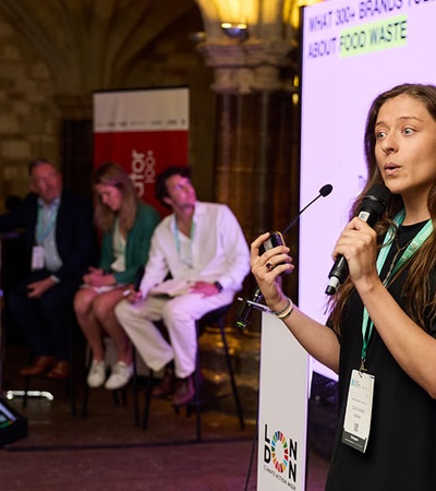 A woman is speaking at a conference about food waste while an audience listens.