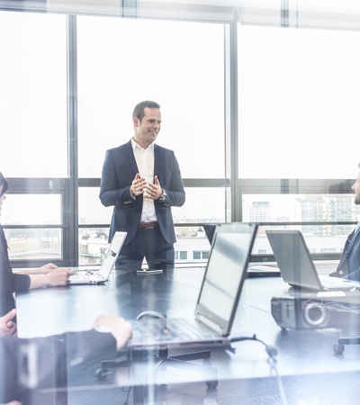 A business meeting in a bright office with a man standing presenting to seated colleagues.