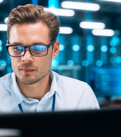 A man with glasses working attentively on a computer in a modern office environment at night.