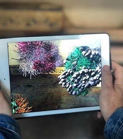 A person holding a tablet displaying colorful, animated 3D objects in a creative setting.