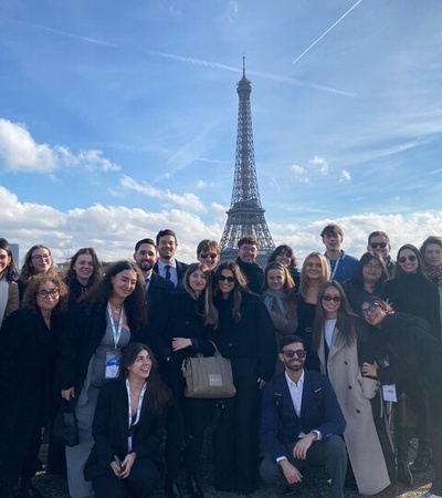 A large group of people posing together in front of the Eiffel Tower on a clear day.