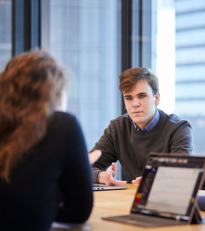 A young man is engaged in a conversation with a woman in a modern office setting.