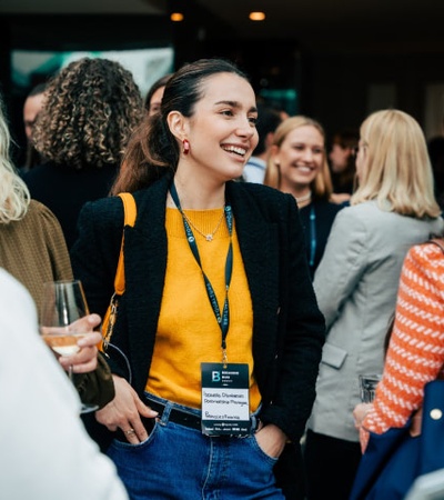 A woman with a lanyard smiling and socializing at a networking event.
