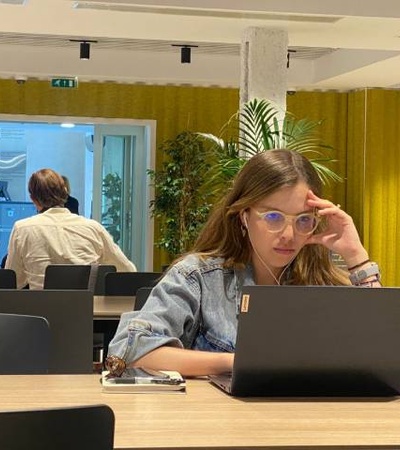 A young woman is focused on her laptop in a bright, modern workspace.