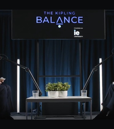 Two men are seated in modern chairs, engaging in a conversation with microphones in a well-lit studio.