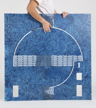 A person holding a large square artwork featuring a symmetrical blue and white abstract design.
