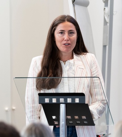 A woman is giving a speech at a podium in front of an audience.