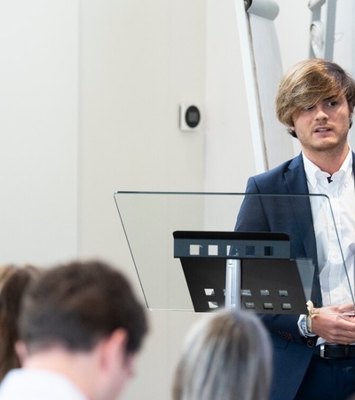 A man with glasses presenting in front of an audience at a seminar.