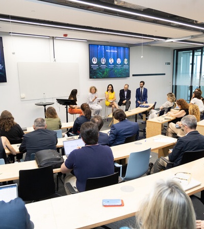 A panel discussion taking place in a modern classroom setting with attendees seated and taking notes.