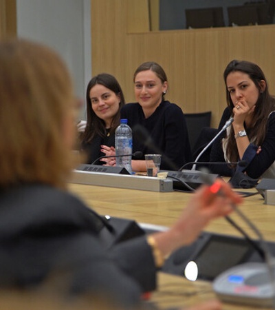 A group of attentive young women listening to a speaker in a conference room.