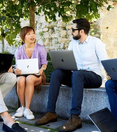 Four professionals sitting outdoors engaged in a discussion with laptops.